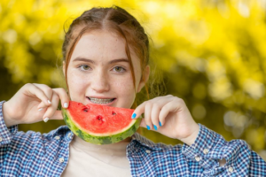 Woman with braces smiling and holding watermelon close to her mouth